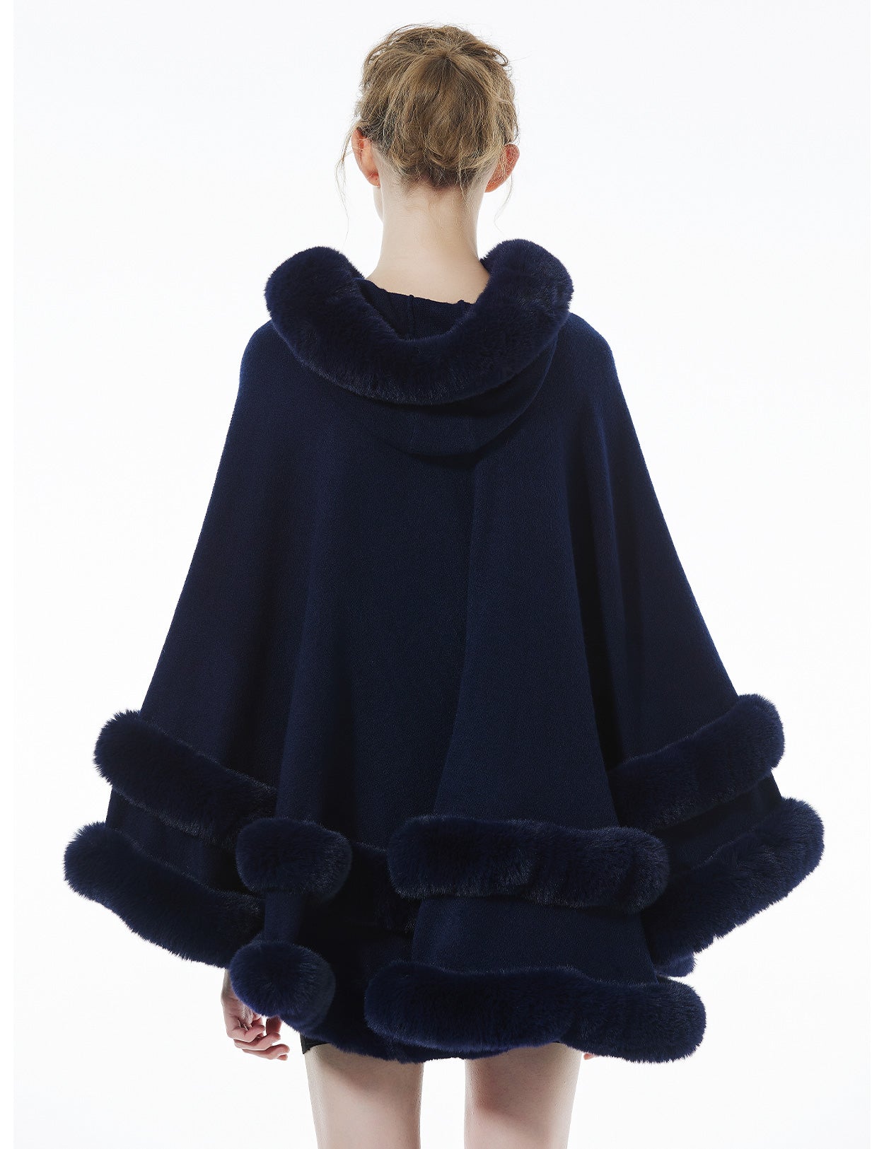 Back view of dark blue hooded knit cape displaying flowing silhouette and faux fur hood detail