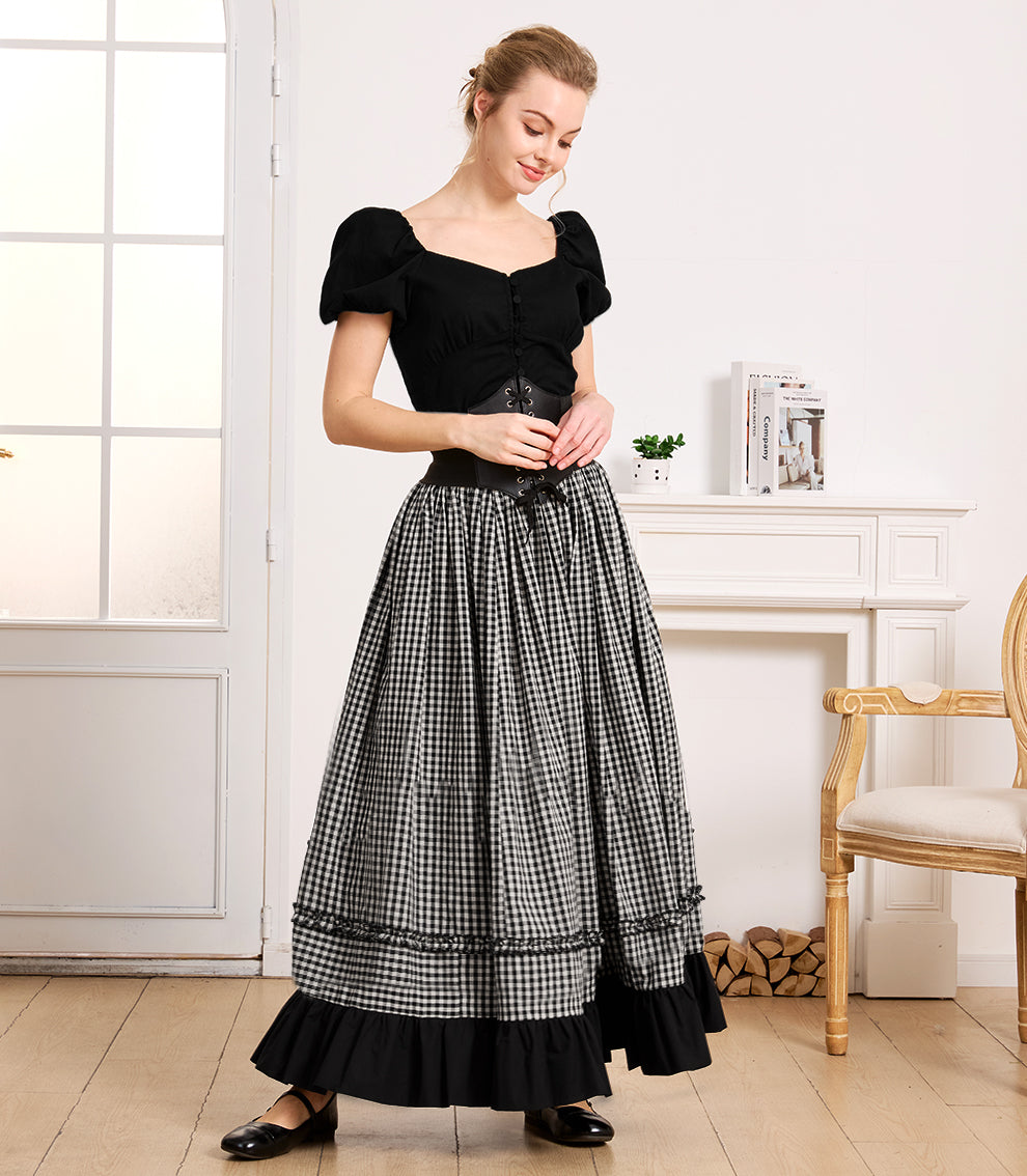 Full-length view of a woman in a bright room setting, elegantly styling a versatile black and white gingham cotton ruffled skirt with a black top and corset belt.