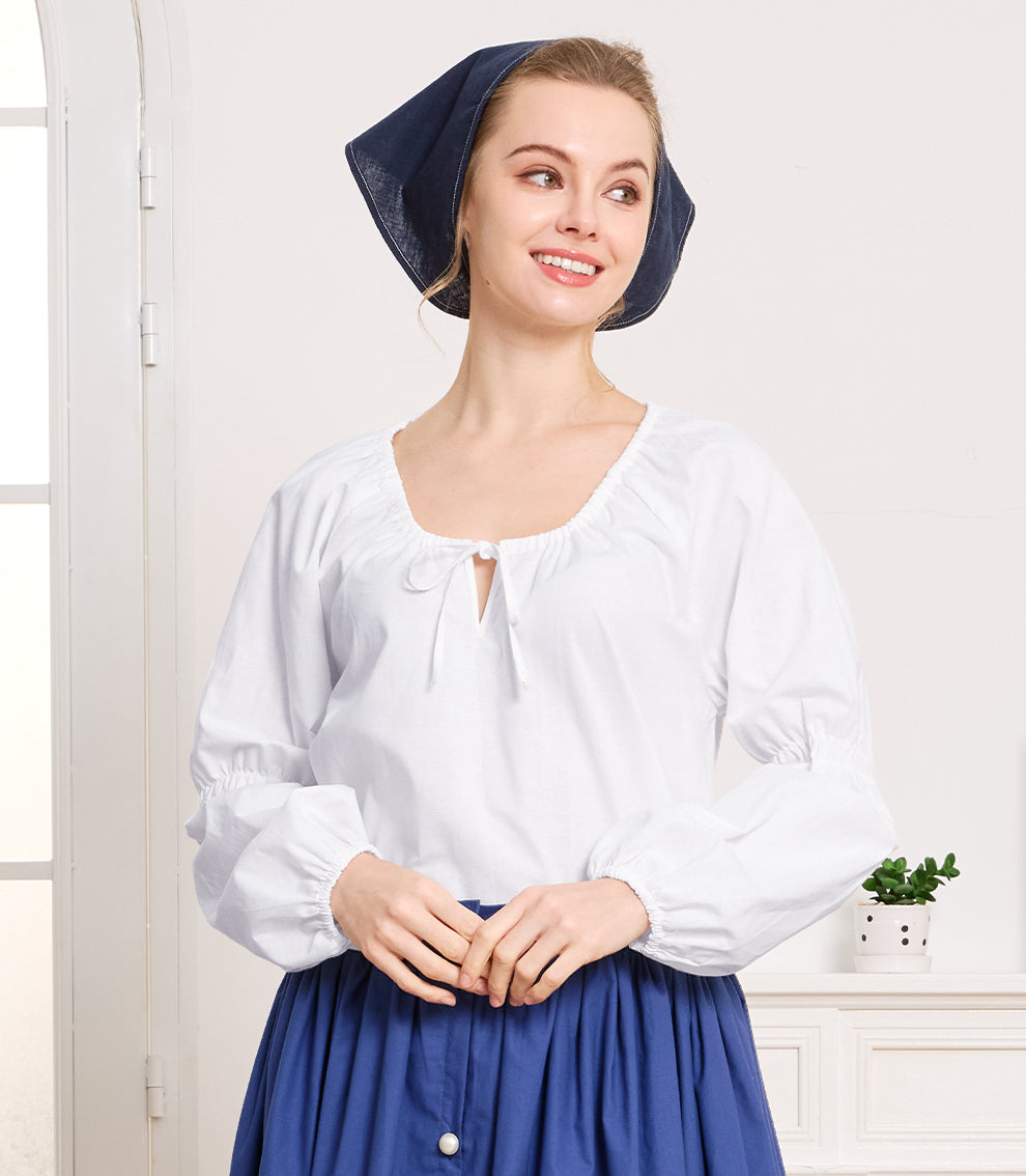 Lifestyle shot of a historical ivory cottagecore blouse paired with a blue vintage skirt and headscarf in a bright room.